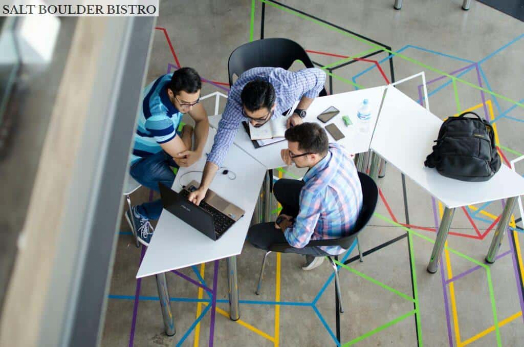 Three men collaborating over a laptop in a modern, geometric-themed office space.