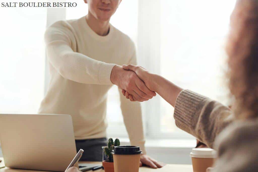 Close-up of professionals shaking hands over coffee in a modern office.