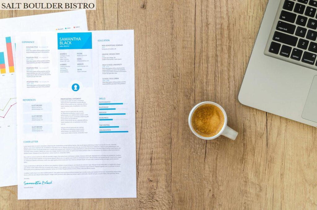 Top view of a desk with resume, coffee cup, and laptop on a wooden surface, ideal for business concepts.