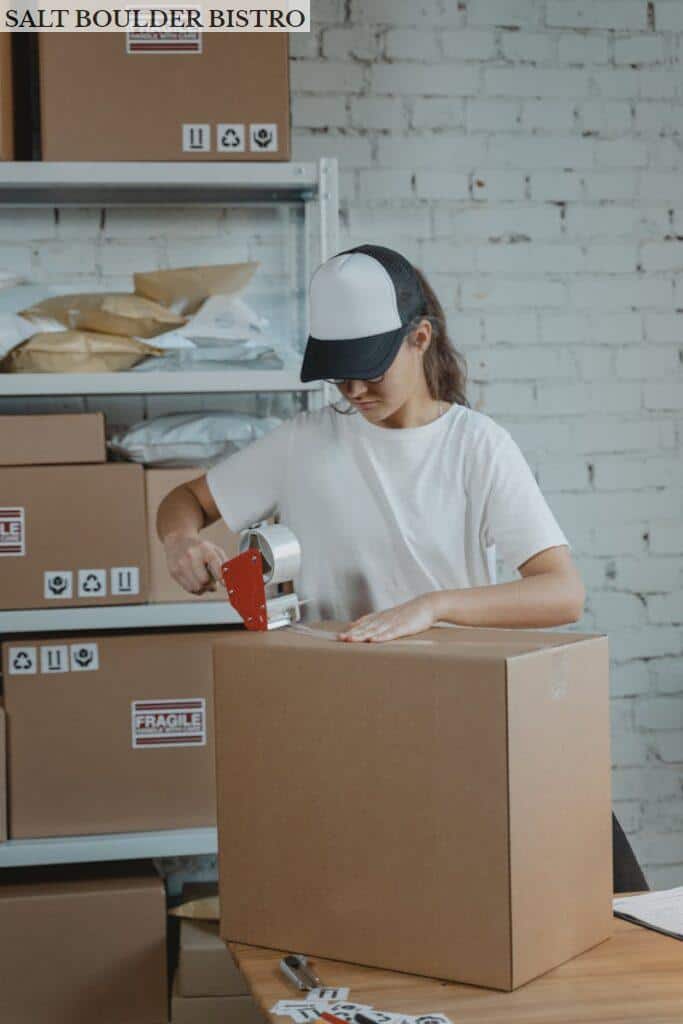 Young female worker sealing cardboard boxes in an indoor warehouse setting.